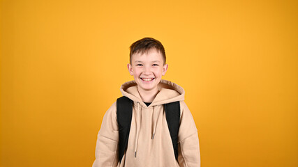 Portrait of adorable boy smilling and looking at camera. Handsome young boy 10s in streetwear hoodie isolated on yellow background studio. People emotions, lifestyle concept.