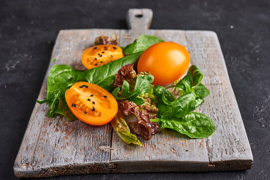 Ingredients for dieting salad - tomatoes, arugula, spinach, lettuce on wooden cutting board on dark background, selective focus, cloce up