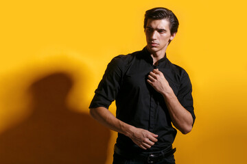 Closeup portrait of a confident young man with hairstyle in black clothing, posing in profile over yellow background.