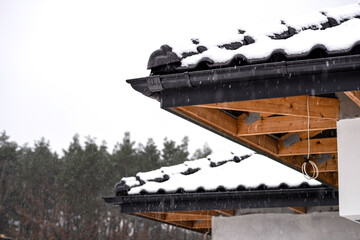 The corner of the roof of a single-family house is covered with snow against the cloudy sky, the...
