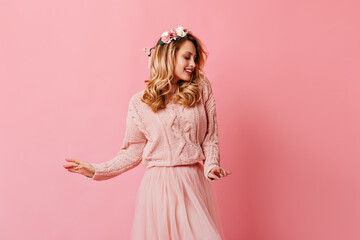 Adorable curly blonde girl in pink skirt and sweater dancing. Woman with flowers in her hair posing...