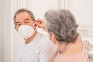 Senior woman putting on surgical mask on her elderly husband during the coronavirus epidemic