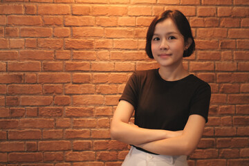 A short haired asian woman wearing a black shirt is smiling on brick wall