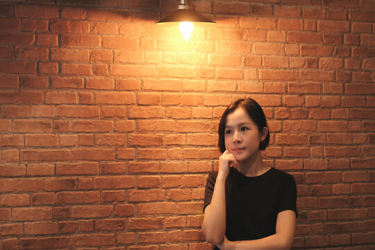 A Short Haired Asian Woman Wearing A Black Shirt Is Thinking Something On Brick Wall