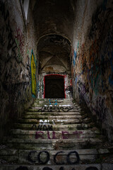 Abandoned dark horror staircase in an old building with graffitis and mysterious doorway at the top