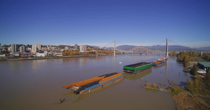 Aerial 4K Island in Fraser River with green trees city of new westminster in background blue sky bright sunny day boats moored and Patullo Bridge