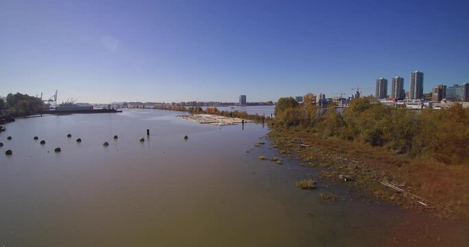 Aerial 4K Island in Fraser River with green trees city of new westminster in background blue sky bright sunny day