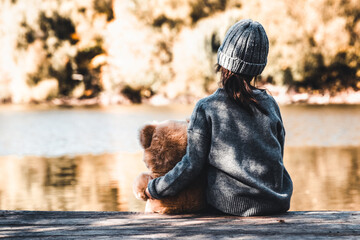 Little girl with taddy bear sit on a shore.