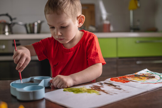 Child in a red T-shirt paints with colorful watercolors at the table