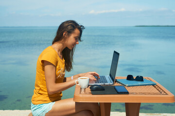 Side view summer freelancer woman working on laptop computer by blue sea during her travel.Technology and travel. Working outdoors