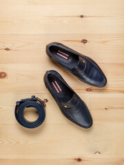 Men's shoes and a trouser belt made of dark blue leather on a wooden background, top view