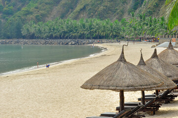 Сomfortable sun loungers on the golden sand under the palm trees of a secluded bay of an island connected to the mainland by a cable car.