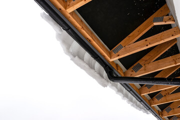 The roof of a single-family house is covered with snow, visible roof trusses from the bottom and a hanging cap of snow on the gutter.