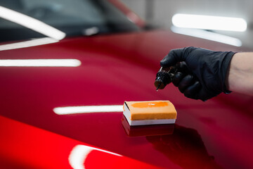 Close-up of a man hand dripping liquid coating on a sponge applicator on a car bonnet. Preparing for applying special coating on a car surface. - 410154826
