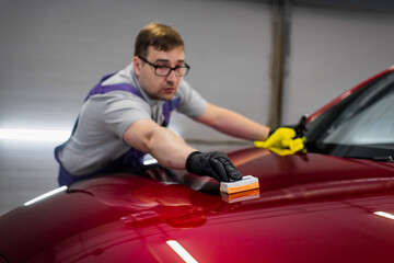 Man worker of car detailing studio applying ceramic coating on car paint with sponge applicator