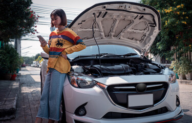 A woman standing next to a car with a bonnet opened and using a cell phone to contact a mechanic to...
