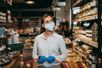 Fototapeta na wymiar Beautiful young and elegant woman with face protective mask and gloves buying healthy food and drink in a modern supermarket or grocery store. Pandemic or epidemic lifestyle and consumerism concept.