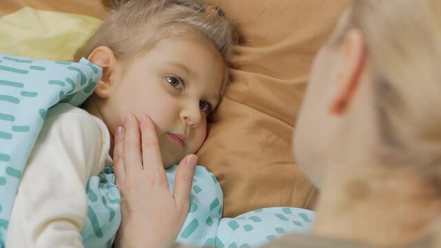 Mom next to lying on the bed with a cute little daughter, stroking the baby's face with her hand.
