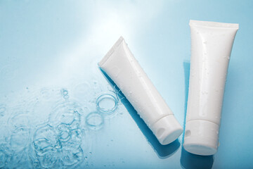 White cosmetic products in tubes on color blue background with water drops. Mock up skincare...