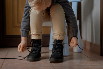 Preschooler child learning to tying shoelace sitting on the chair at home, selective focus. Step by step instruction. Step 3 
