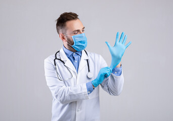 Professional doctor in medical mask putting on gloves over grey studio background. Prevention of...