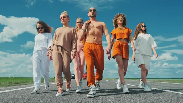A group of brutal stylish hipsters are walking along the road against the background of the summer sky. The concept of successful beautiful confident people.