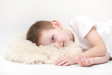 Obraz na płótnie Canvas portrait of a happy cute little boy waking up in the morning and lying on a white pillow isolated on a white background. fresh and cozy bedding sheets. Bedtime for kids. concept of happy dreaming