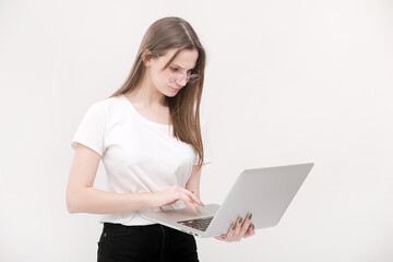 Naklejka premium Portrait of a beautiful young girl with blond hair in glasses and a white T-shirt working or studying on a laptop isolated on a white background. Concept of business woman. Casual blogger woman