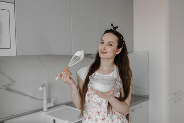 Cute girl in apron whisking eggs and smiling while baking in the kitchen at home on easter...