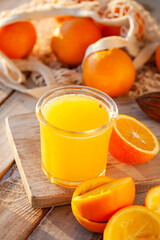 Glass of freshly sqeezed orange juice on a wooden table. Natural source of vitamins, healthy beverage for ideal breakfast. Bright sunny summer day. Close up, copy space for text.