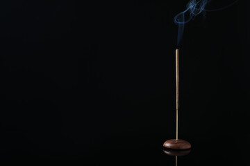 Incense stick smoldering in holder on black background. Space for text