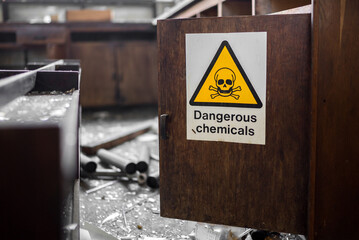 Yellow triangle with black skull and crossbones dangerous chemicals sign on open wooden cupboard door in abandoned laboratory after burglary equipment vandalised by thief