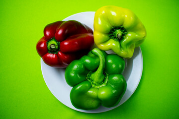 bright colored bell peppers on white plate on green background