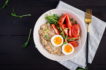 Breakfast oatmeal porridge with boiled egg, cherry tomatoes and microgreens. Healthy balanced food. Top view, above, copy space
