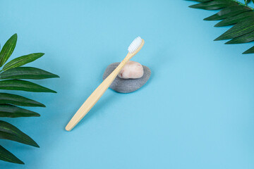 Fototapeta na wymiar Ecological bamboo toothbrush on stone, tropical leaves on a blue background. Zero waste concept. Sustainable lifestyle. Plastic-free concept. copy space. top view