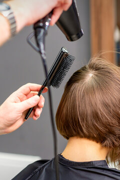 Hairdresser dries brown hair of the young woman in a beauty salon