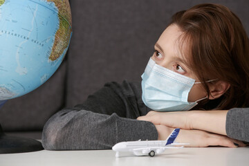 Traveling during coronavirus outbreak. Portrait of young woman with disposable protection mask and plane toy, daydreaming about traveling around globe.