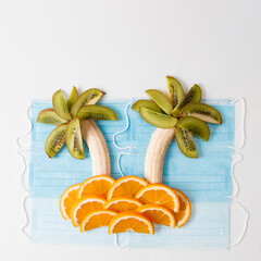 Palm tree island concept Corona art from kiwi, banans and oranges on sugical mask as ocean water