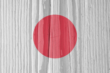 The flag of Japan on a dry wooden surface, cracked with age. Light pale faded paint. Patriotic background or wallpaper. Hinomaru, flag of sun. Annual rings of old wood. Direct sunlight with shadows
