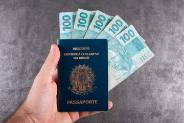 Hand holding Brazilian passport with one hundred reais bills