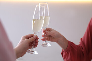 Women clinking glasses of champagne indoors, closeup. Holiday cheer and drink