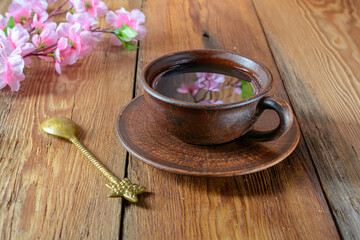 A cup of tea with a reflection of a cherry twig on a dark textured wooden table.Selective Focus.The concept of recreation.
