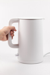 a female hand holds a white electric kettle by the handle on a white wooden table background