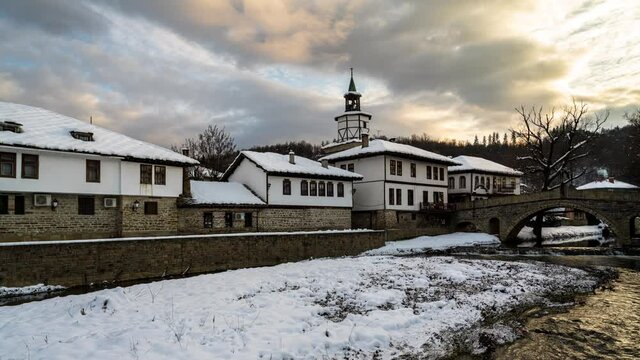 Time lapse before sunset with moving clouds over old houses covered with snow in the revival architectural complex in Tryavna, Bulgaria, 4K Time lapse.