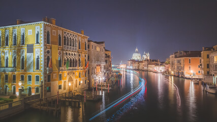 A view of the Grand Canal at night and illuminated white dome of Basilica di Santa Maria della Salute in Venice, Italy with lights trails from passing boats.