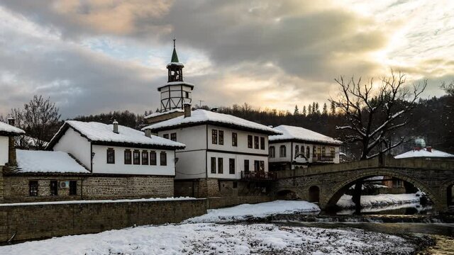 Time lapse before sunset with moving clouds over old houses covered with snow in the revival architectural complex in Tryavna, Bulgaria, 4K Time lapse.