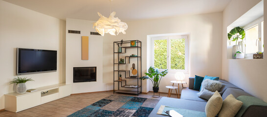 Panorama of wide modern living room with design sofa and large pillows above. Design library and small fireplace