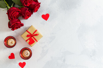 St. Valentine's Day background with product place or copy space. Small hearts, candles, a gift and red roses bouquet on light concrete background. Romantic love background. Happy Valentines Day.