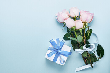 Pink roses flowers bouquet with ribbon and gift box over beautiful blue background. Greeting card template with copy space