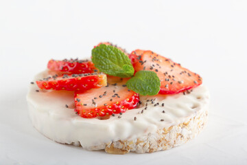 Puffed exploded wheat grains with white chocolate frosting with chopped strawberries, chia seeds and mint leaves on a light wooden background. Close-up